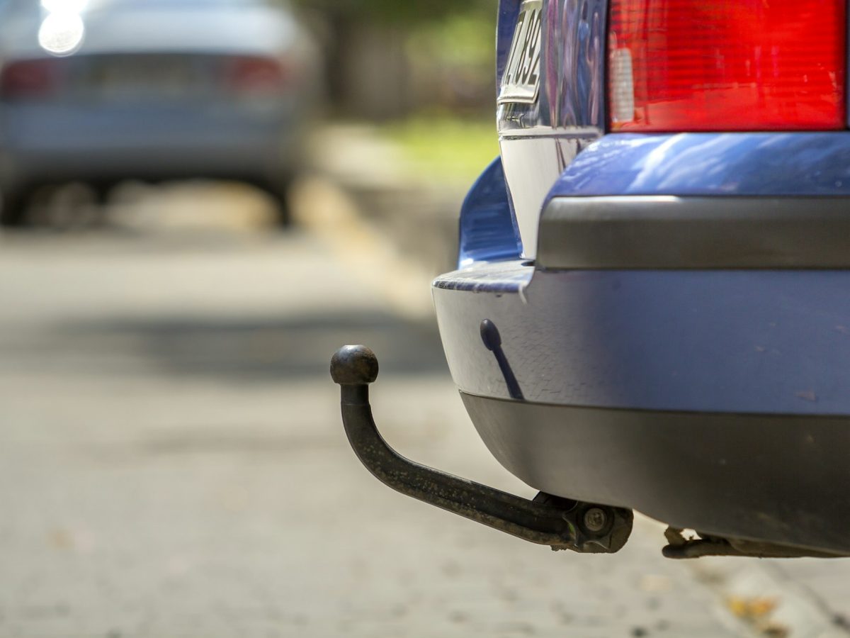 Blue car parked on sunny street, red stop lights, hook for dragging trailer, tow hitch or towbar